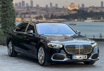 Luxury black executive car (Maybach S-Class) with a blurred Istanbul Bosphorus skyline view in the background. Vehicle used for Istaur's private rental services.